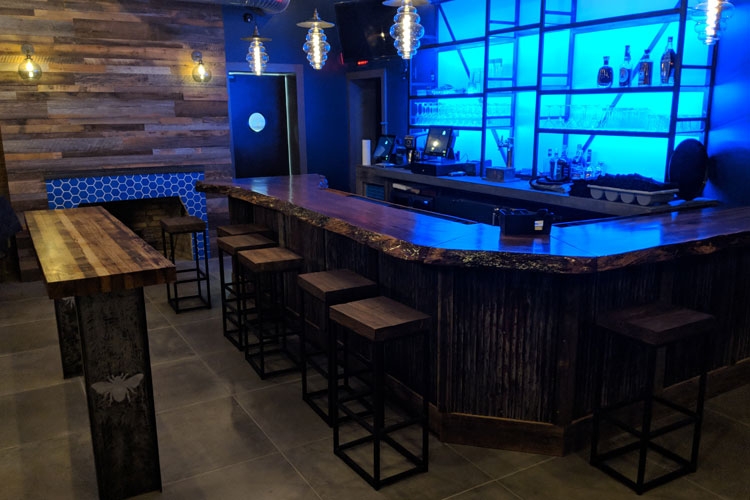 Bar Area: Steel and reclaimed barnwood bar table, Live-edge oak bar with concrete inlay detail and reclaimed metal face, Steel and glass back bar with custom lighting, Reclaimed barnwood fireplace accent wall